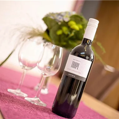 A bottle of Austrian wine is on a table, surrounded by wine glasses. In the background, fresh flowers can be seen.