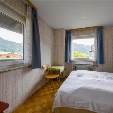 Ein gemütliches Schlafzimmer mit einem großen Bett und einem Tisch. Durch die Fenster hat man einen schönen Blick auf die Berge.