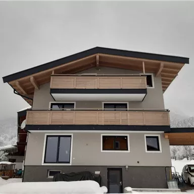 Ein modernes Haus mit einem schneebedeckten Dach und Balkonen. Die Umgebung ist winterlich und ruhig.