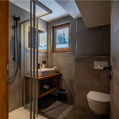 Ein modernes Badezimmer mit einer Dusche und einem Waschbecken aus Holz. Große Fliesen und ein Fenster sorgen für eine helle Atmosphäre.