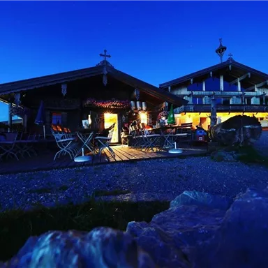 A mountain hut at night, illuminated by warm light. Surrounded by a peaceful, rural landscape.