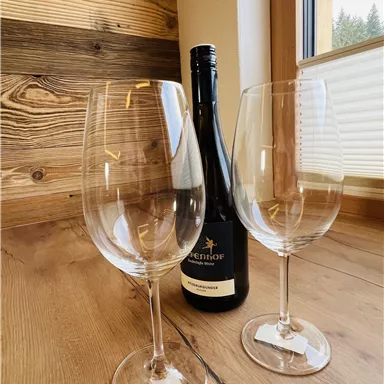 Zwei Weingläser stehen auf einem Holztisch neben einer Flasche Wein. Die Fenster bieten einen Blick nach draußen.
