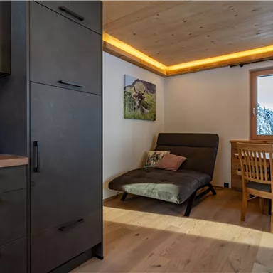 Ein modernes Zimmer mit Holzböden und einer gemütlichen Sitzecke. An der Wand hängt ein Bild und ein Fenster bietet Blick auf die Umgebung.
