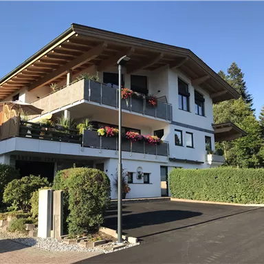 A modern house with a balcony and colorful flowers. Surrounded by green shrubs and trees.