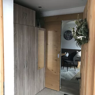An entrance area with wooden cabinets and an open door to a bright room. The walls are neutral and the floor is tiled.