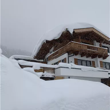 Ein modernes Chalet inmitten einer schneebedeckten Landschaft. Der Himmel ist grau, und der Schnee liegt hoch auf dem Boden.