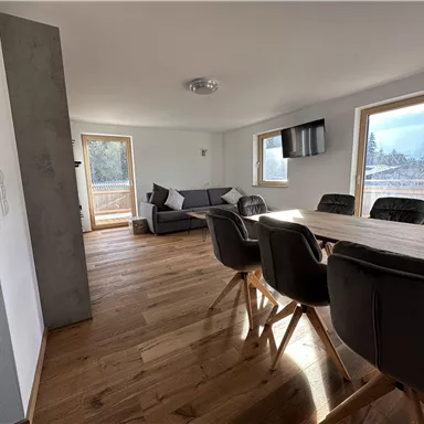 Ein helles und modernes Wohn- und Esszimmer mit Holzboden. Es gibt große Fenster und eine komfortable Couch.