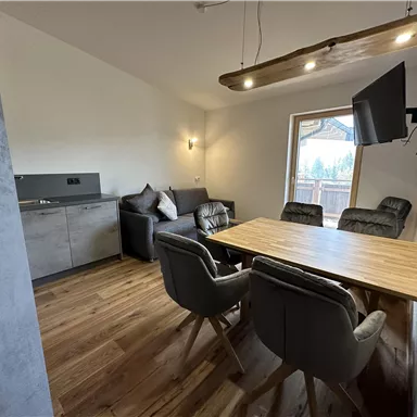 Ein modernes Wohnzimmer mit einem offenen Essbereich. Es gibt einen Tisch mit Stühlen, eine gemütliche Couch und einen Fernseher an der Wand.