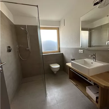 Ein modernes Badezimmer mit einer Dusche, einem Waschbecken und einem Fenster. Die Wände sind in neutralen, grauen Tönen gehalten.