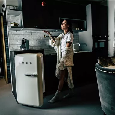 A person is standing in a modern kitchen and juggling an apple. The room feels stylish and cozy, with a striking refrigerator and elegant furniture.