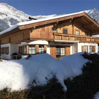 Ein schönes Chalet im Schnee mit Bergen im Hintergrund. Die Veranda und Fenster sind aus Holz und strahlen Gemütlichkeit aus.