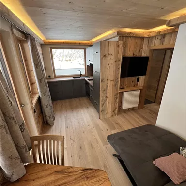 Ein modernes Wohnzimmer mit Holzverkleidung und großen Fenstern. Der Raum ist gemütlich eingerichtet mit einem Esstisch und einer Sofaecke.