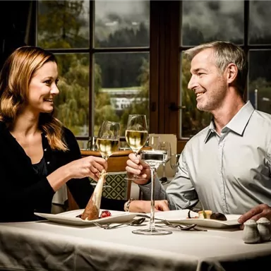 A romantic dinner by candlelight. A couple toasts with glasses and enjoys the meal in an elegant setting.