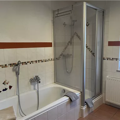 Ein modernes Badezimmer mit einer Badewanne und einer separaten Dusche. Die Wände sind gefliest und es gibt ein Fenster für Tageslicht.