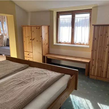 Ein helles Schlafzimmer mit einem Doppelbett und Holzschränken. Das Zimmer hat große Fenster, die natürliches Licht hereinlassen.