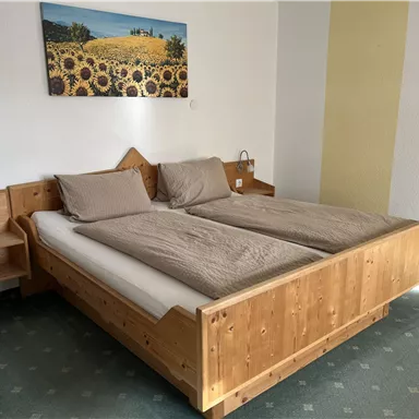 Ein gemütliches Schlafzimmer mit einem großen Holzbett und zwei Kissen. An der Wand hängt ein Bild von Sonnenblumen, und es gibt Nachttische mit Lampen.