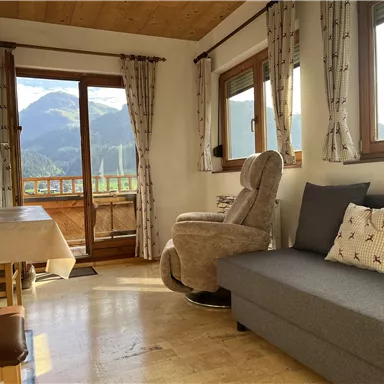 Ein gemütliches Wohnzimmer mit Blick auf die Berge. Es gibt einen grauen Sofa, einen Fernseher und einen bequemen Sessel.