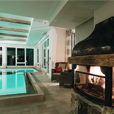 Ein moderner Innenraum mit einem Pool und einem gemütlichen Kamin. Große Fenster lassen viel Licht herein und bieten eine entspannende Atmosphäre.