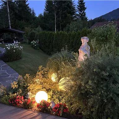 A beautiful garden in the evening light with colorful flowers and a statue. Soft lighting creates an inviting atmosphere.