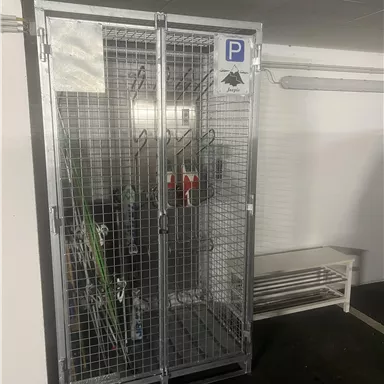 A secure bike parking room with grids and a parking sign. Inside, some bicycles and accessories can be seen.