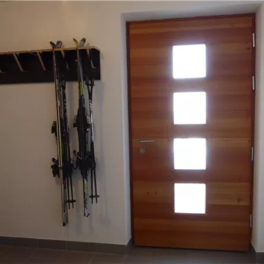 A modern entrance area with a wooden panel door and three windows. Ski poles hang on the wall, ready for the next trip.
