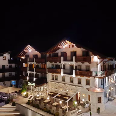 Ein elegantes Hotelgebäude bei Nacht, beleuchtet von warmen Lichtern. Moderne Architektur mit gemütlichem Ambiente und Außenbereich.
