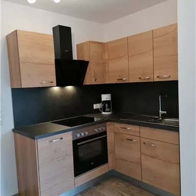A modern kitchen with wooden cabinets and a dark countertop. It includes a stove, a cooktop, and a sink.
