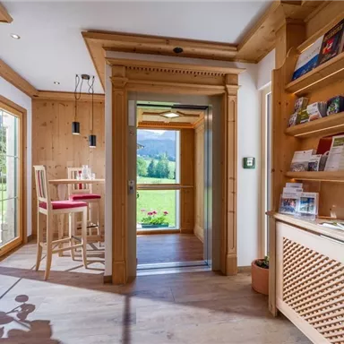 Ein gemütlicher Empfangsbereich mit Holzverkleidung und hellen Möbeln. Durch die Fenster ist eine grüne Landschaft sichtbar.