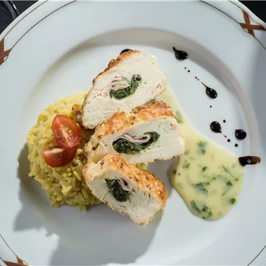 A delicious dish with stuffed chicken breast fillet, served with yellow rice and cherry tomatoes. Accompanied by a creamy sauce and a flavorful puree.