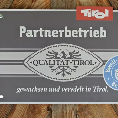 A sign with the inscription "Partnerbetrieb" and the logo "Qualität Tirol". It attests to products that have been grown and refined in Tyrol.