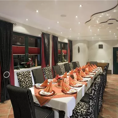 Ein eleganter Speisesaal mit einem langen Tisch, der mit servierten Tellern und dekorierten Servietten gedeckt ist. Die Wände sind mit stilvollen Vorhängen geschmückt und die Beleuchtung sorgt für eine gemütliche Atmosphäre.