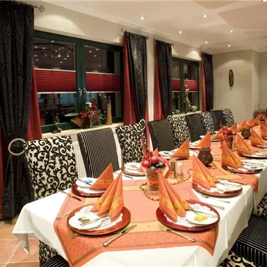 Ein elegant gedeckter Tisch in einem stilvollen Restaurant. Die Dekoration umfasst orangefarbene Servietten und ein einladendes Ambiente.