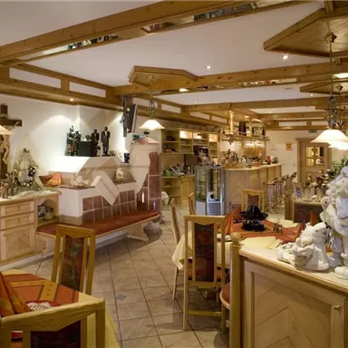 Ein gemütliches Restaurant mit Holzverzierungen und warmem Licht. Die Tische sind ordentlich gedeckt und eine Bar ist sichtbar im Hintergrund.