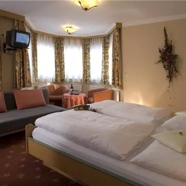 Ein gemütliches Schlafzimmer mit zwei Betten, einem Sofa und Fenstern, die viel Licht hereinlassen. Die stilvolle Einrichtung sorgt für eine einladende Atmosphäre.