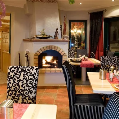 Ein gemütliches Restaurant mit einem offenen Kamin. Die Tische sind festlich gedeckt und die Einrichtung ist modern mit eleganten Stühlen.