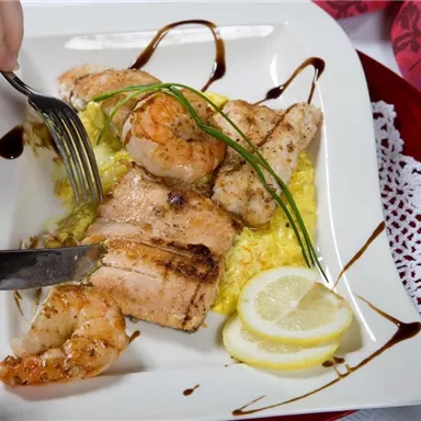 Ein appetitliches Gericht mit gegrilltem Fisch und Garnelen auf einem Bett aus gelbem Reis. Frische Zitronenscheiben und Kräuter garnieren den Teller.