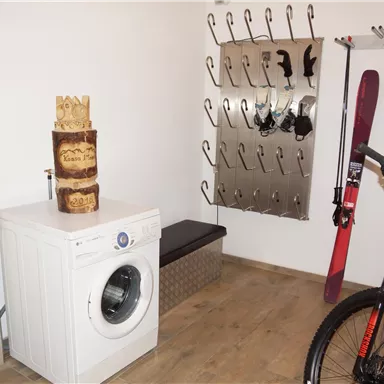Ein praktischer Raum mit einer Waschmaschine, einem Fahrrad und Skier an der Wand. Der Boden ist aus Holz und bietet eine gemütliche Atmosphäre.