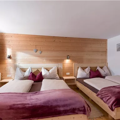 Ein gemütliches Schlafzimmer mit drei Betten und Holzverkleidung. Die Kissen und Decken in lila Farben verleihen dem Raum einen einladenden Touch.