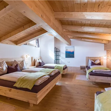 Ein gemütliches Schlafzimmer mit Holzbalken und mehreren Betten. Die Einrichtung ist schlicht und einladend, mit grünen Decken und einem bunten Bild an der Wand.