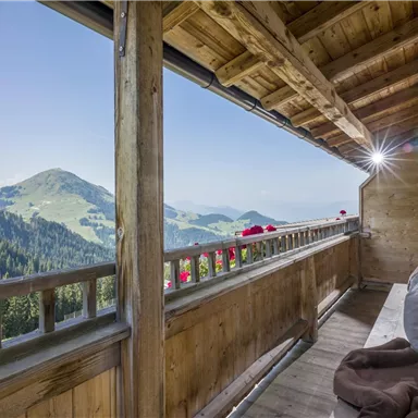 Ein Holzbalkon mit einem schönen Blick auf grüne Hügel und Berge. Die Umgebung ist sonnig und einladend.