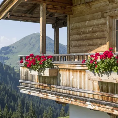 Ein Holzhaus mit einem Balkon, der mit roten Blumen verschönert ist. Im Hintergrund sind grüne Berge und ein klarer Himmel sichtbar.