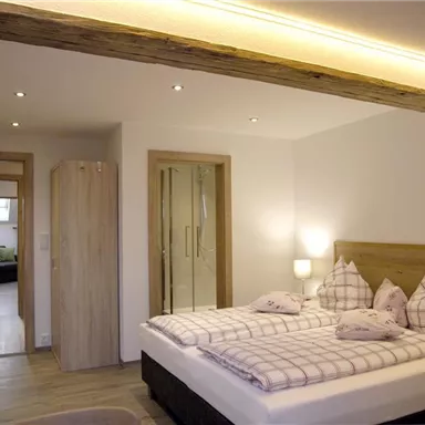 A modern bedroom with a large bed and a bright, inviting atmosphere. In the background, additional rooms are visible, creating a cozy home vibe.