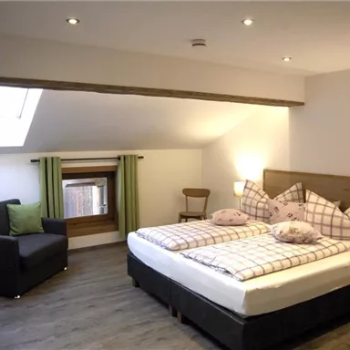 A cozy bedroom with a double bed and soft pillows. There is a seating area and plenty of daylight through a window.