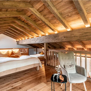 Ein gemütliches Schlafzimmer mit einem Holzfußboden und einer modernen Holzdecke. Ein bequemes Bett und ein Stuhl mit einem kleinen Tisch schaffen eine einladende Atmosphäre.