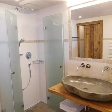 Ein modernes Badezimmer mit einer geräumigen Dusche und einer eleganten Waschschüssel aus Stein. Die Wände sind hell und die Ausstattung wirkt stilvoll und einladend.