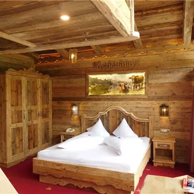 Ein gemütliches Zimmer mit Holzmöbeln und einem großen Bett. Die Wände sind aus Holz und es gibt ein paar Fenster mit natürlichem Licht.
