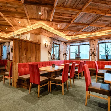 Ein einladendes Restaurant mit Holzmöbeln und roten Sitzbänken. Der Raum ist gemütlich beleuchtet und bietet große Fenster mit Blick nach draußen.