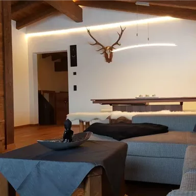 Ein gemütliches Wohnzimmer mit Holzverkleidung und modernen Lichtelementen. Ein bequemes Sofa und ein dekorativer Tisch verleihen dem Raum eine einladende Atmosphäre.
