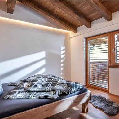 Ein gemütliches Schlafzimmer mit Holzdecke und einem großen Fenster. Das Bett ist mit karierten Kissen und Decken dekoriert.