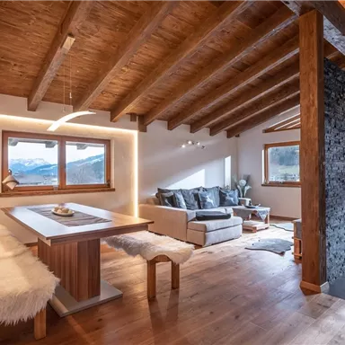 Ein modernes Wohnzimmer mit Holzdecke und großem Fenster. Es bietet eine gemütliche Atmosphäre mit einem Esstisch und einer bequemen Sitzecke.